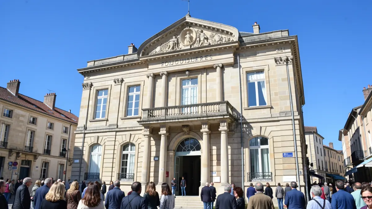 Facade of the Bruguières town hall, a stone building with a balcony, under a bright blue sky.