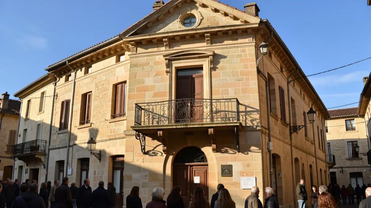 Stone facade of the Saint-Affrique town hall with ornate iron balcony and railings, warm afternoon sunlight casting shadows on the sandstone walls, blue sky.